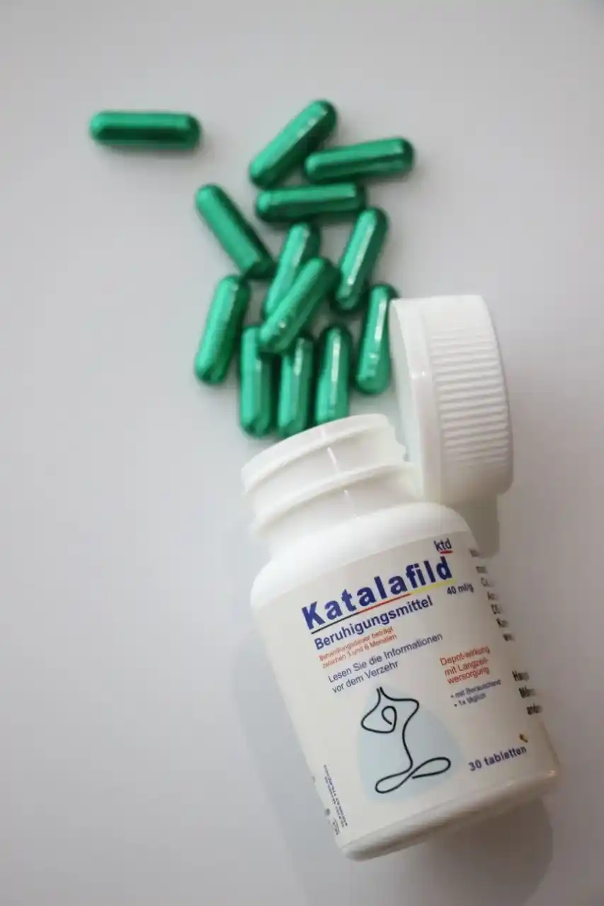 دوز 40 قرص کاتالافیلد با درب باز قوطی ریخته روی سطح سفید با کپسول های سبز رنگ